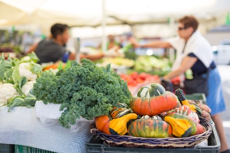 Farmers' food market stall with variety of organic vegetable. Vendor serving and chating with customers.の写真素材