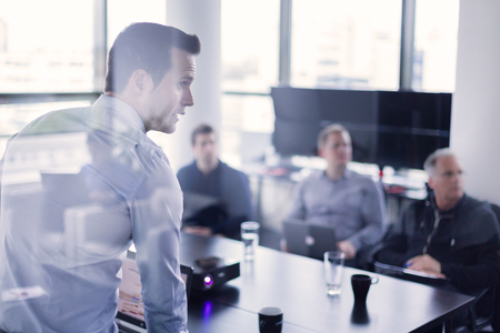 Business man making a presentation at office. Business executive delivering a presentation to his colleagues during meeting or in-house business training, explaining business plans to his employees. Business man making a presentation at office. Business executive delivering a presentation to his colleagues during meeting or in-house business training, explaining business plans to his employees.