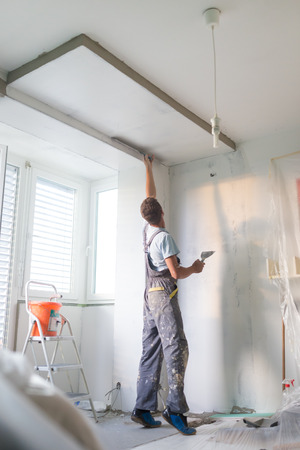 Thirty years old manual worker with wall plastering tools inside a house. Plasterer renovating indoor walls and ceilings with float and plaster.の写真素材