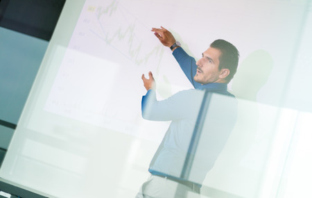 Business man making a presentation in front of whiteboard. Business executive delivering a presentation to his colleagues during meeting or in-house business training. View through glass.の写真素材