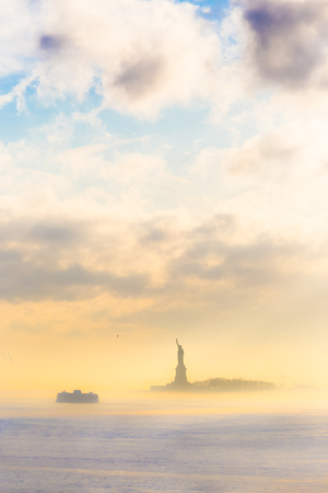 Staten Island Ferry cruises past the Statue of Liberty on a misty sunset. Manhattan, New York City, United States of America. Vertical composition. Copy space.の写真素材
