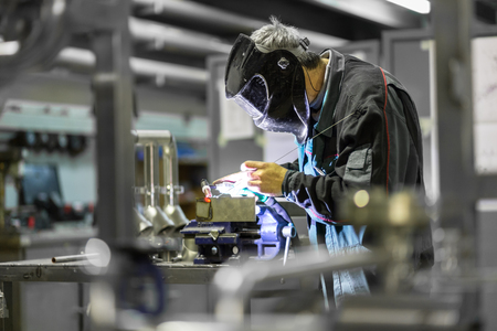 Industrial worker with protective mask welding inox elements in steel structures manufacture workshop.