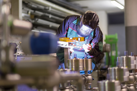 Industrial worker with protective mask welding inox elements in steel structures manufacture workshop.