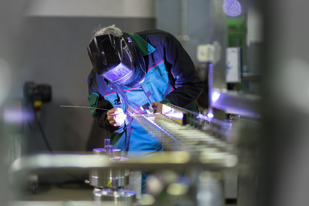 Industrial worker with protective mask welding inox elements in steel structures manufacture workshop.