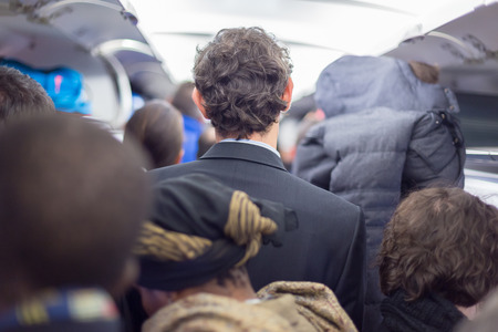 Interior of airplane with passengers queuing on the aisle, collecting their luggage to disembark plane.の写真素材