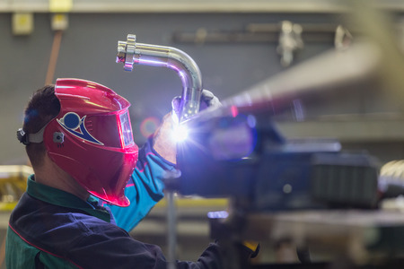 Industrial worker with protective mask welding inox elements in steel structures manufacture...