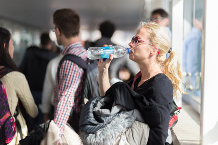Young blond caucsian woman drinking water while waiting in queue to board plane.の写真素材