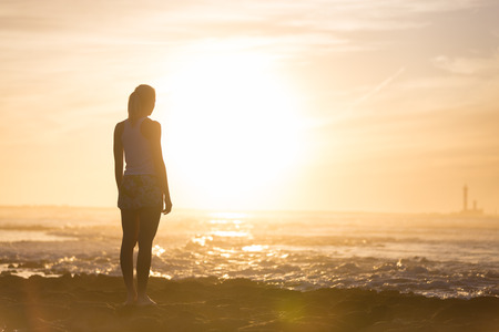 Silhouette of meditative, sensual blonde woman watching sunset at the beach.の写真素材