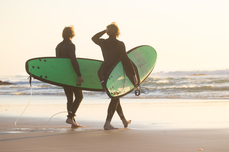 Male surfers on sandy beach with the surfboard in sunset.の写真素材