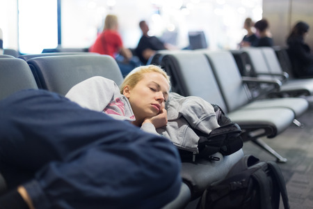 Tired female traveler sleeping on the airpot departure gates bench with all her luggage by her side.  Tireing travel concept.の写真素材