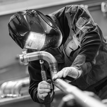 Industrial worker with protective mask welding inox elements in steel structures manufacture...