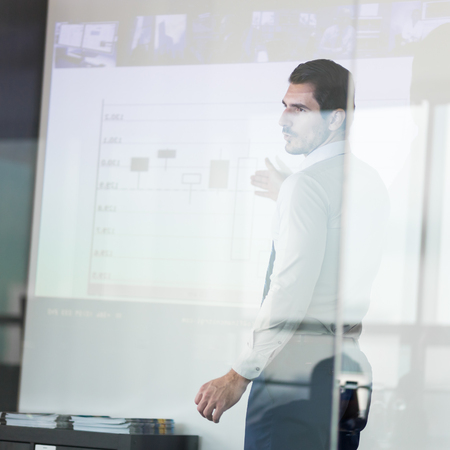 Business man making a presentation in front of whiteboard. View through glass.