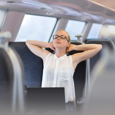 Businesswoman traveling by train, streching on her seat while working on laptop. Business travel...
