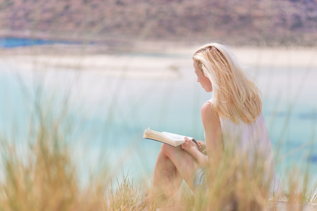 Relaxed woman enjoying sun, freedom and good book an beautiful sandy beach of Balos in Greece. Young lady reading, feeling free and relaxed. Vacations, freedom, happiness, enjoyment and well being.の写真素材