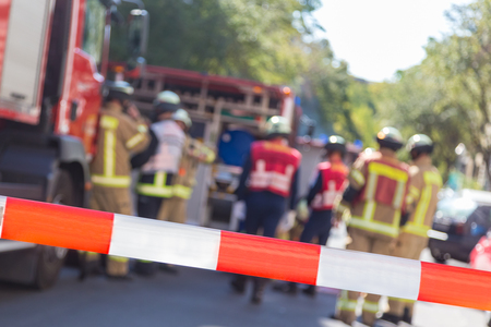 Team of blured firefighters by firetruck on protected accident site. Focus on red and white security...