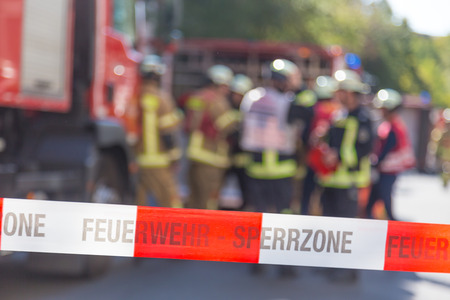 Team of blured firefighters by firetruck on protected accident site. Focus on red and white security...