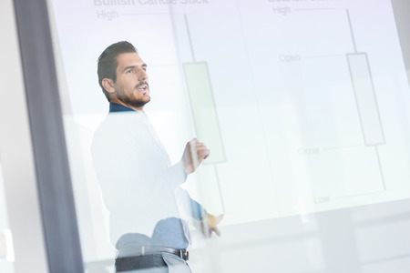 Business man making a presentation in front of whiteboard. Business executive delivering a presentation to his colleagues during meeting or in-house business training. View through glass.の写真素材
