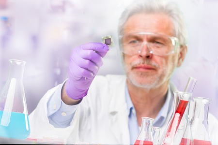 Focused senior life science professional holding and observing the micro chip.  Lens focus on the...