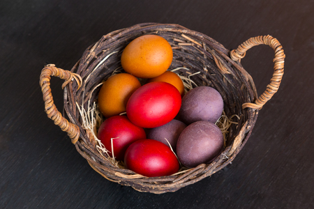 Wicker basket with colorful Easter eggs on wooden table, closeupの写真素材