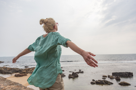 Free woman enjoying windy weather on beach on overcast day with arms raised outstretched.の写真素材