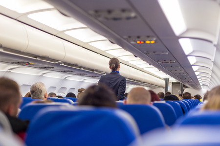 Interior of airplane with passengers on seats and stewardess walking the aisle.の写真素材