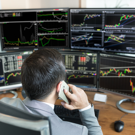 Over the shoulder view of and stock broker trading online while accepting orders by phone. Multiple...