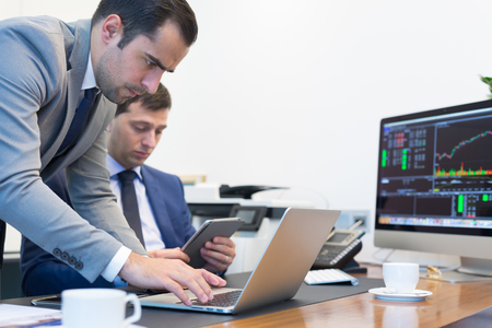 Image of two young businessmen solving business issue using laptop computer and touchpad at business meeting in moder office.の写真素材