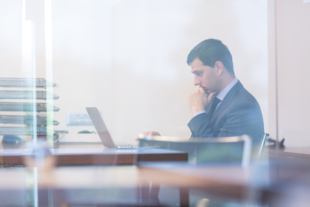 Elegant businessman analyzing data on laptop computer in modern office.の写真素材