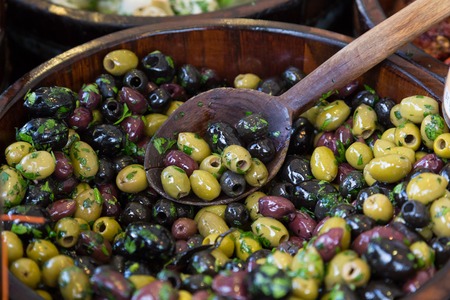 Olives with serving spoons in wooden bowls being sold on local grocery market.の写真素材