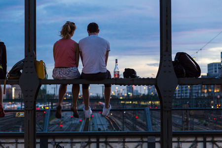 Young couple in love on romantic date sitting on railway bridge with a bottle of wine and watching the sunset over Munich urban city center. Just the two of us.の写真素材