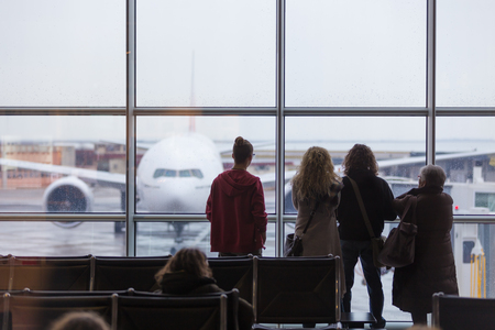 People waiting for airplane departure at the airport gates on a rainy day. Bad rainy weather with storms and strong winds causing delays in air traffic.の写真素材
