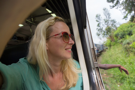 Blonde caucasian woman looking trough old retro blue train window , traveling by train in third...