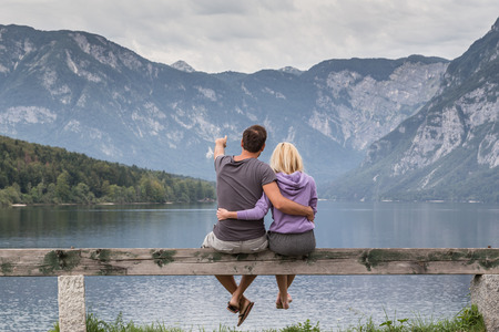 Embraced casual couple watching tranquil overcast morning scene at lake Bohinj, Alps mountains, Slovenia.の写真素材