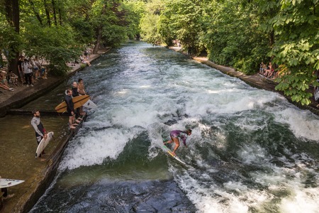 Munich, Germany, June 24, 2015: Surfers practicing their skill on an artificial wave situated on Isar river channel in Englischer garten, Munich central park, on 24th of June, 2015 in Munich, Germany.のeditorial素材