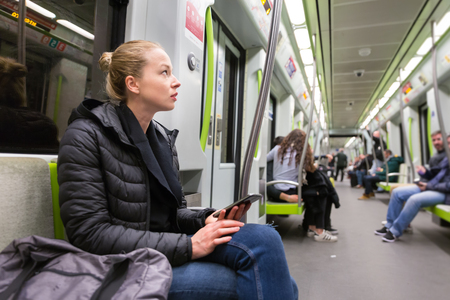 Young girl holding mobile phone while traveling on metro. Wireless internet on public transport concept.の写真素材