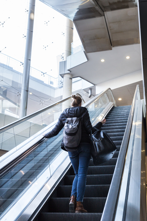 Young businesswoman with large black bag and mobile phone getting up the escalator during business trip in modern city.の写真素材