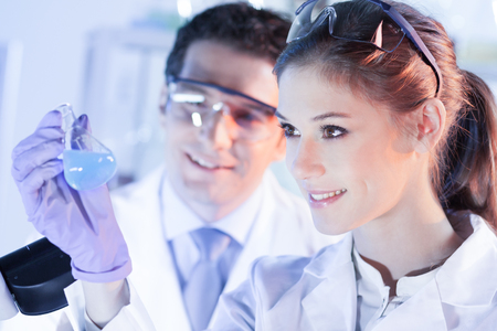 Chemical laboratory. Attractive young PhD student and her post doctoral supervisor scientist observing the blue indicator color shift after the solution destillation.の写真素材
