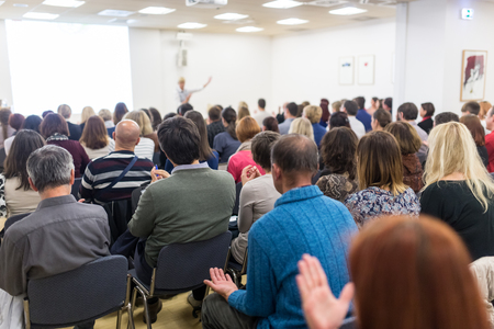 Life coaching symposium. Female speaker giving interactive motivational speech at entrepreneurship workshop. Audience in conference hall. Rear view of unrecognized participant.の写真素材