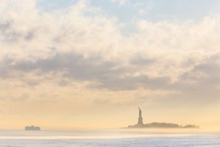 Staten Island Ferry cruises past the Statue of Liberty on a misty sunset. Manhattan, New York City, United States of America. Vertical composition. Copy space.の写真素材