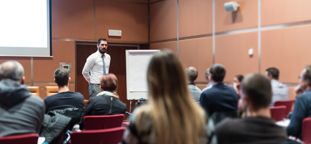 Public Speaker Giving a Talk at Business Meeting. Audience in the conference hall. Skilled coach answers questions of participants of business training. Business and Entrepreneurship concept.の写真素材