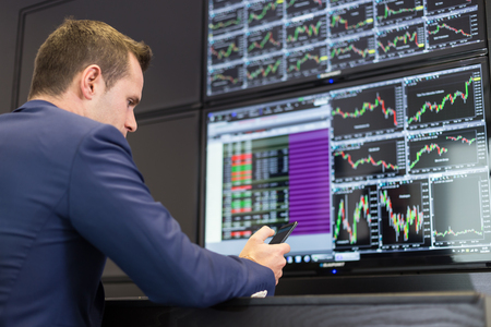Businessman with cell phone trading stocks. Stock analyst looking at graphs, indexes and numbers on...