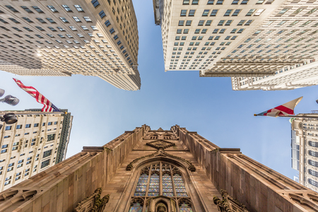Wide angle upward view of Trinity Church at Broadway and Wall Street with surrounding skyscrapers, Lower Manhattan, New York City, USA.の写真素材