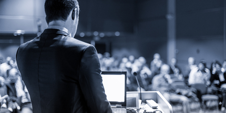 Speaker giving a talk on corporate business conference. Unrecognizable people in audience at conference hall. Business and Entrepreneurship event. Blue toned grayscale image.の写真素材