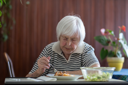 Solitary senior woman eating her lunch at retirement home. Social aid for retirement citizens concept.の写真素材