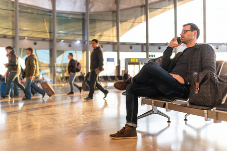 Man talking on his mobile phone while waiting to board a plane at the departure gates at the airport terminal.の写真素材