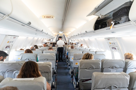 Interior of commercial airplane with unrecognizable passengers on their seats during flight. Steward...
