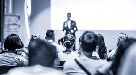 Speaker giving talk at business event. Audience at the conference hall. Business and Entrepreneurship concept. Focus on unrecognizable people in audience. Blue toned grayscale image.の写真素材