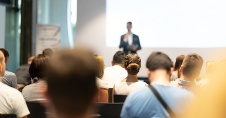 Male speaker giving a talk in conference hall at business event. Audience at the conference hall. Business and Entrepreneurship concept. Focus on unrecognizable people in audience.の写真素材