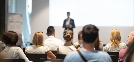 Male speaker giving a talk in conference hall at business event. Audience at the conference hall. Business and Entrepreneurship concept. Focus on unrecognizable people in audience.の写真素材
