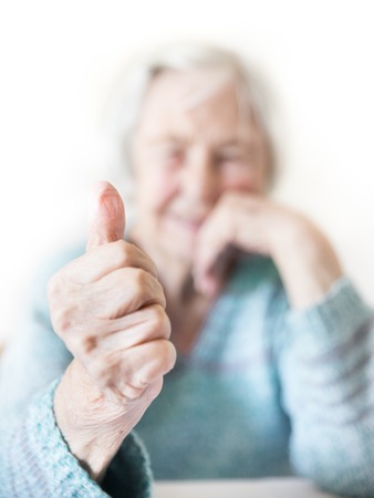 Content 96 years old elderly woman giving a thumb up and looking at camera. Focus on the thumb up, face out of focus. Old age and the quality of life concept.の写真素材